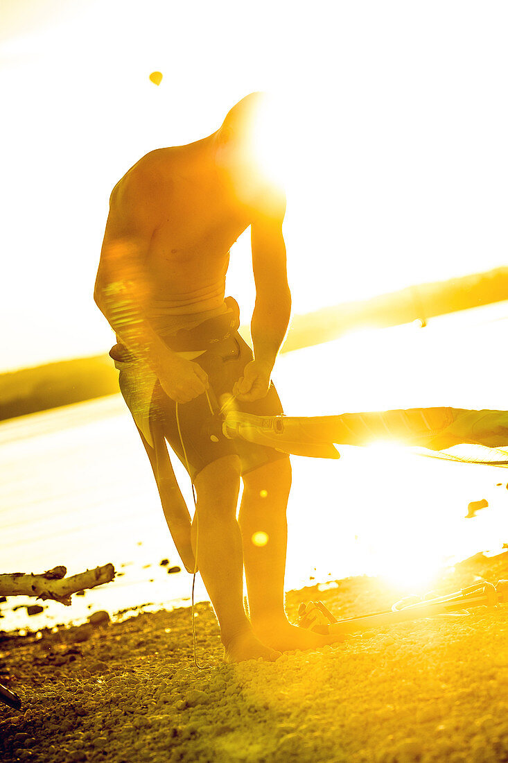 Young male windsurfer trimming his sail at the lake on a sunny day, Ammersee, Bavaria, Germany