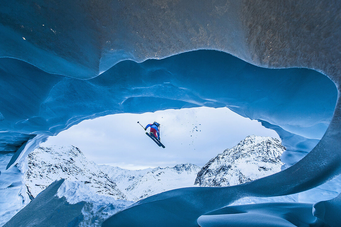 Junge Skifahrerin springt von einer Gletscherhöhle in den Bergen herunter/ Pitztal, Tirol, Österreich