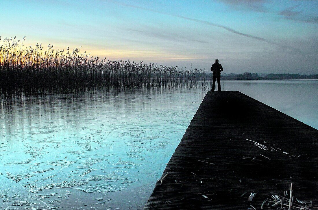 Man standing on jetty, late evening Lough Ennell, County Westmeath, Ireland.