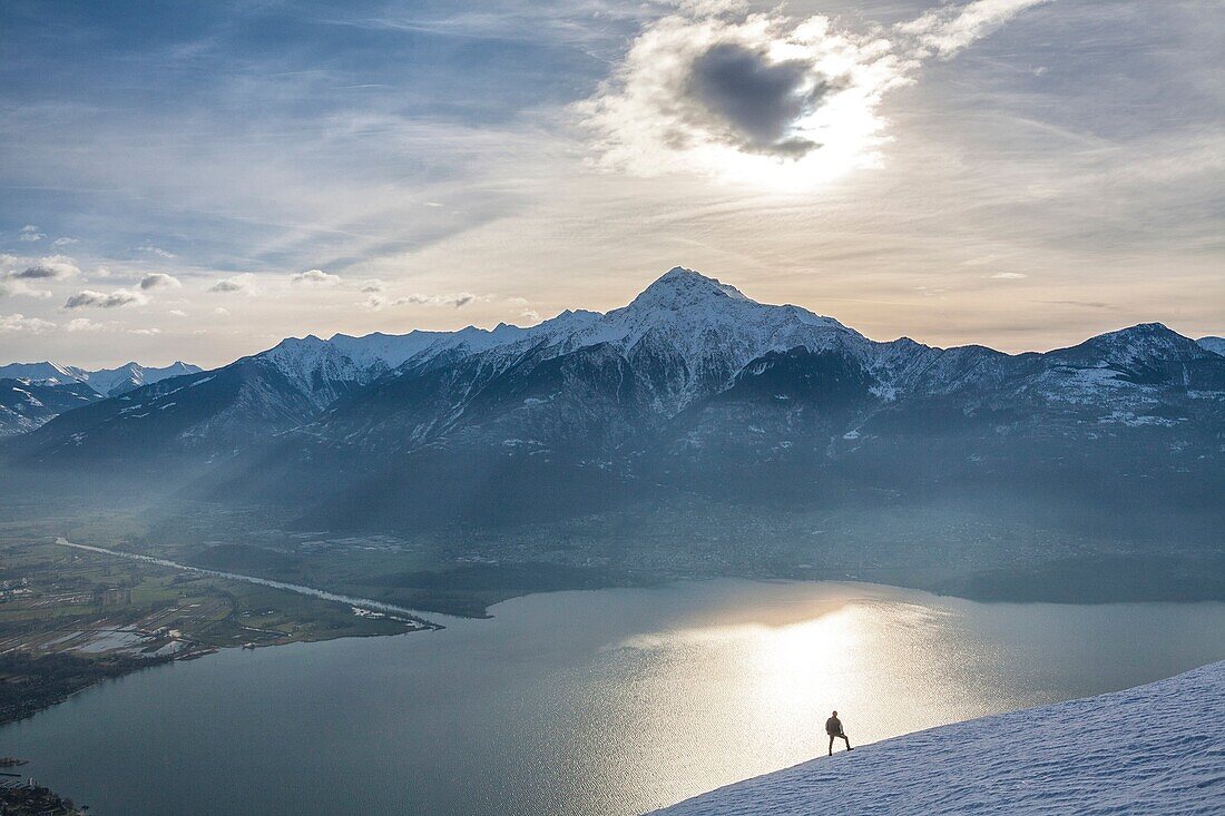 Hiker admires Lake Como and Mount Legnone on a cold winter morning Vercana mountains High Lario Lombardy Italy Europe.