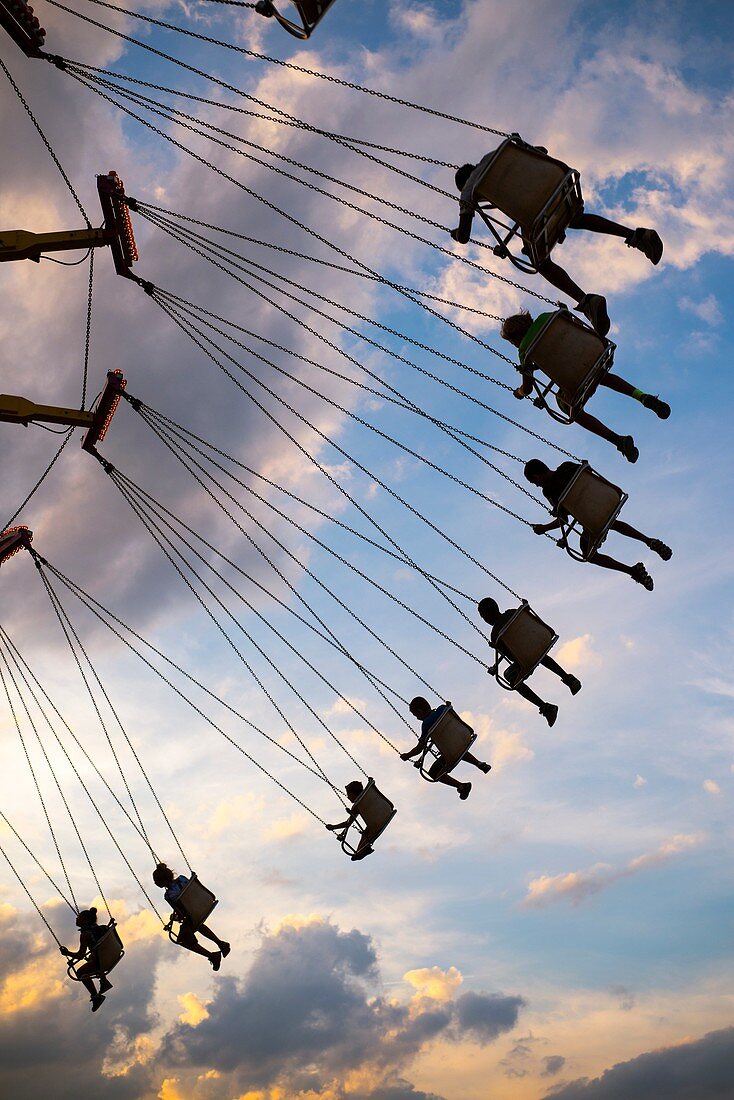 An amusement ride at a county fair sends riders soaring through the air at sunset.