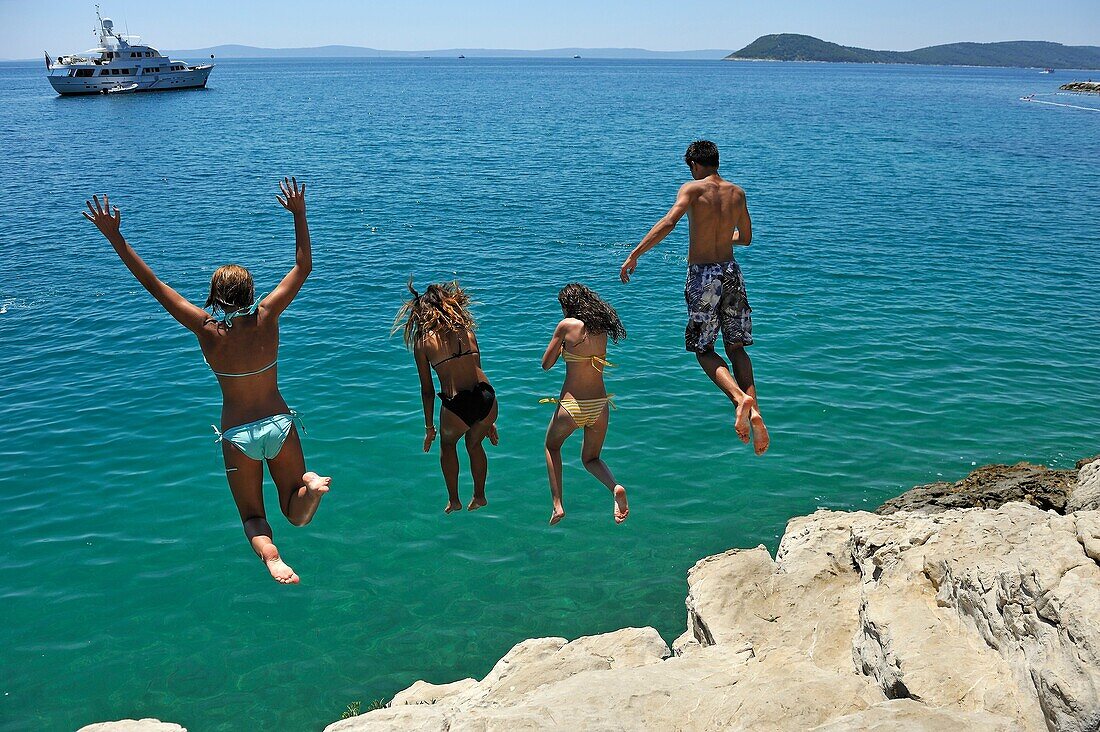 Jugendliche tauchen von den Felsen vor dem Strand Jezinac am Fuße des Marjane-Hügels, Split, Kroatien, Südosteuropa.