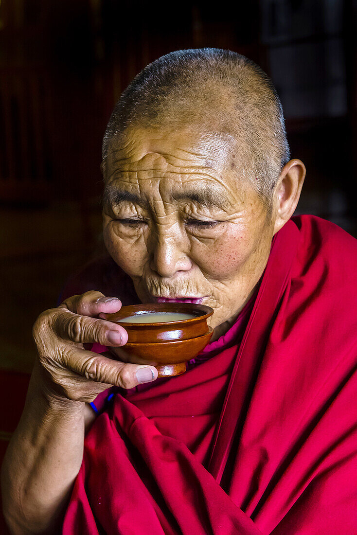 A Buddhist nun drinking yak butter tea, Drepung Monastery, Tibet (Xizang), China.