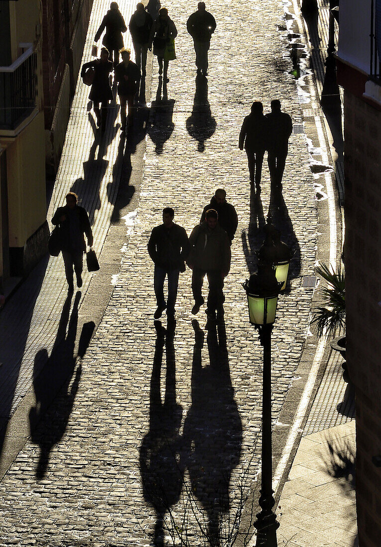 seen from above silhouettes of people walking paved street, strong shadows, old town of Cadiz, Andalusia, Spain