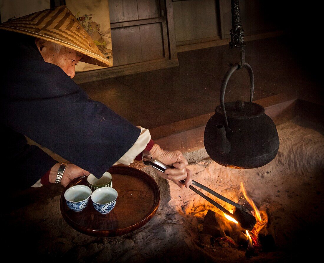 Tea shop owner adds charcoal to fire, ready to make tea for guests, Magome pilgrim trail, old post road between Kyoto and Tokyo, Japan.