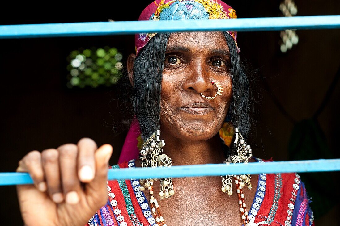 Lambani woman at home near Hampi in Karnataka state, India. She is holding a bar of the window of her house with her hand.