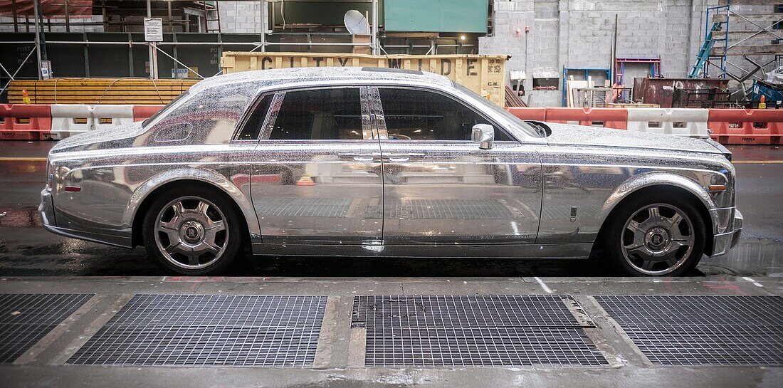 A silver, highly reflective Rolls-Royce automobile is parked in Lower Manhattan in New York