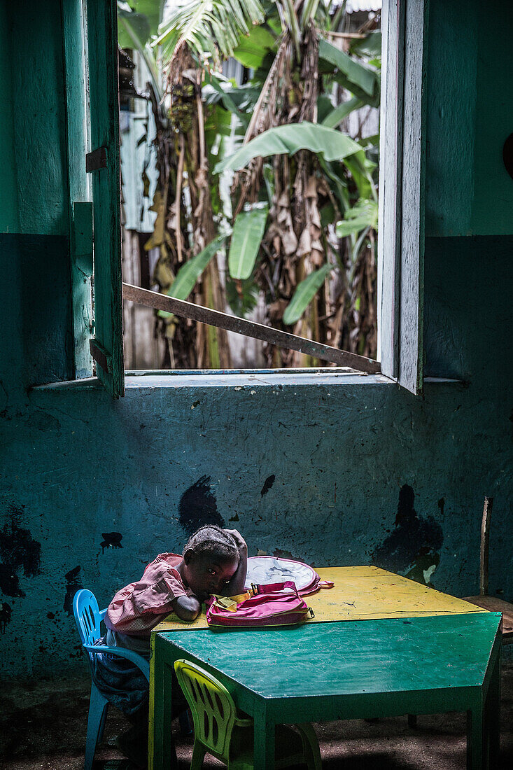 Kleines einheimisches Mädchen stützt ihren Kopf auf einen Tisch in einer ärmlichen Umgebung, Sao Tome, Sao Tome und Príncipe, Afrika