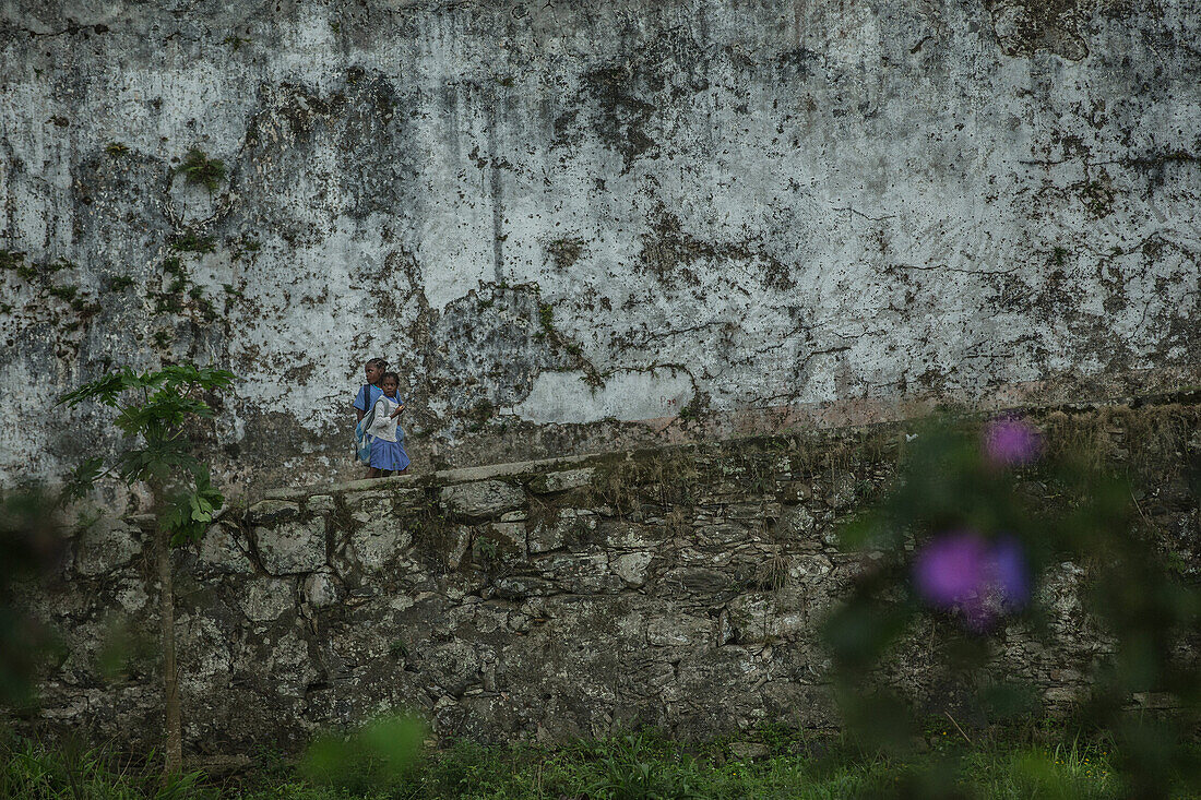 Zwei kleine einheimische Kinder gehen an einer großen Mauer vorbei,  Monte Café, Sao Tomeund Príncipe,  Afrika