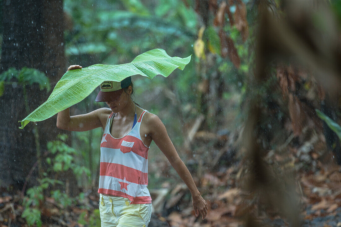 Junge Frau hält ein großes Blatt über ihren Kopf um sich vor dem Regen zu schützen, Sao Tome, Sao Tome und Príncipe, Afrika