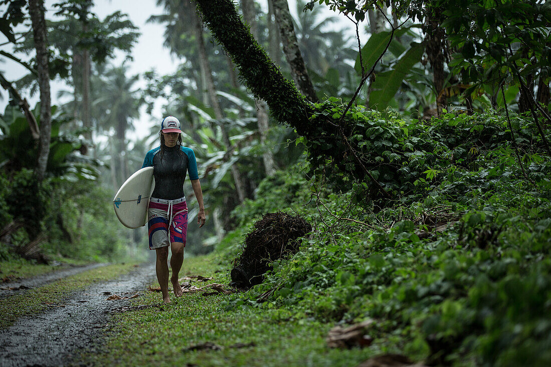 Young female surfer walking on a simple street through a forest, Sao Tome, Sao Tome and Principe, Africa