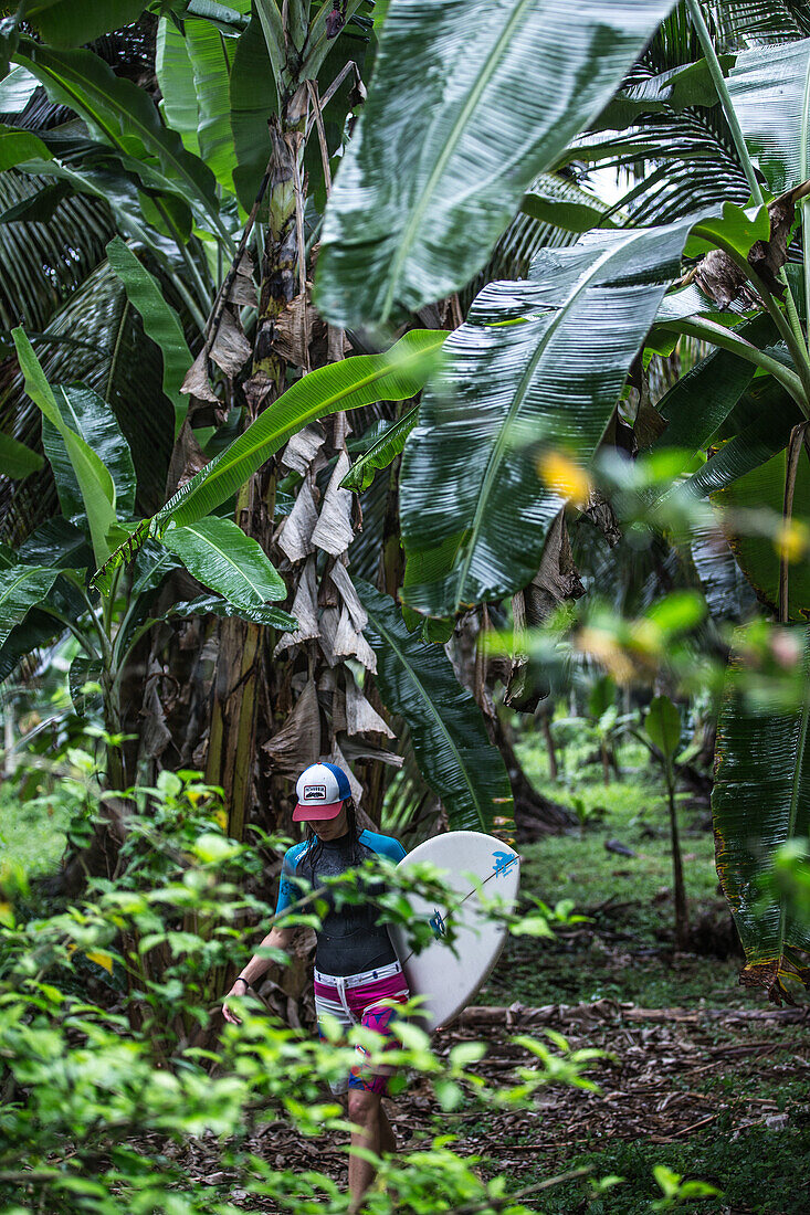 Young female surfer walking through a thick jungle, Sao Tome, Sao Tome and Principe, Africa