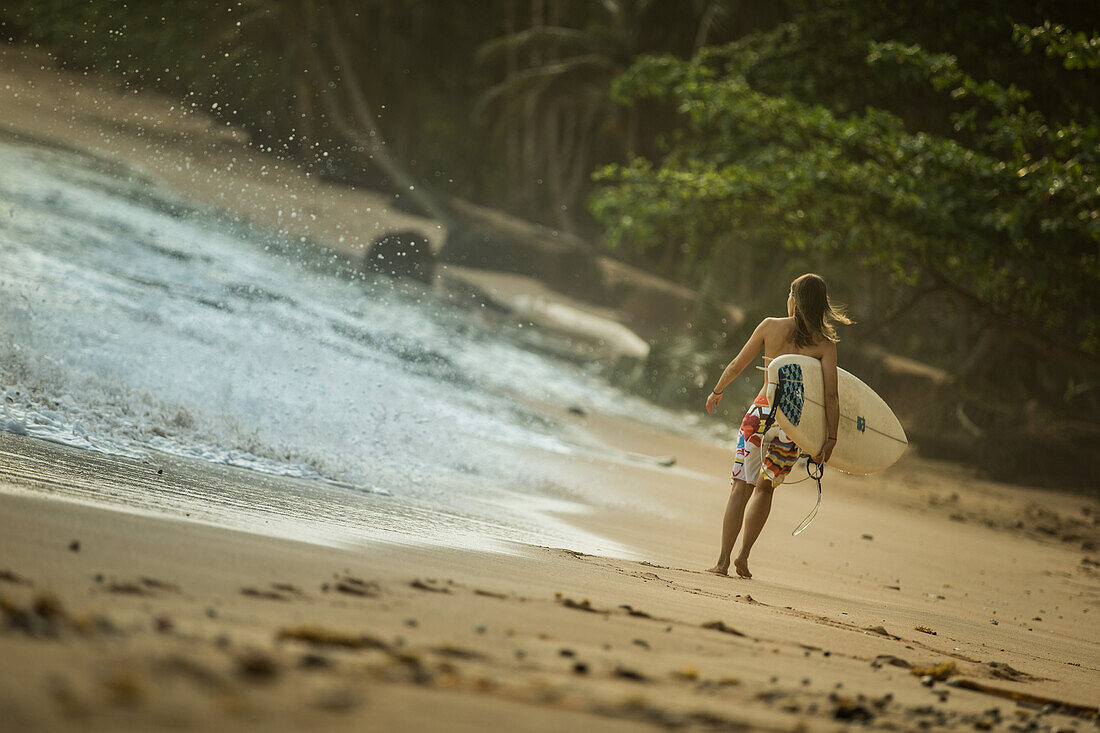 Young female surfer walking along the beach, Sao Tome, Sao Tome and Principe, Africa