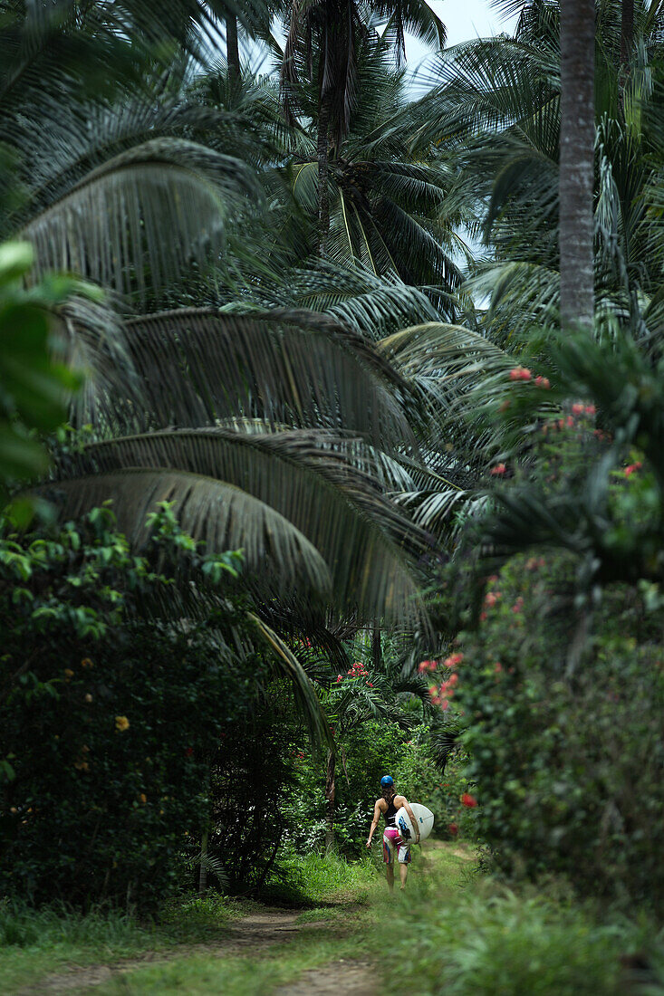 Young female surfer walking on a path through a forest, Sao Tome, Sao Tome and Príncipe, Africa