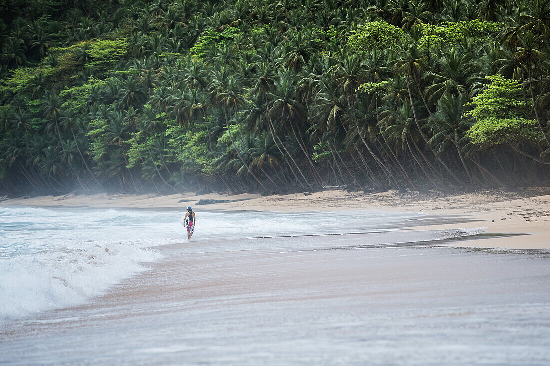 Young female surfer walking along the beach, Sao Tome, Sao Tome and Principe, Africa