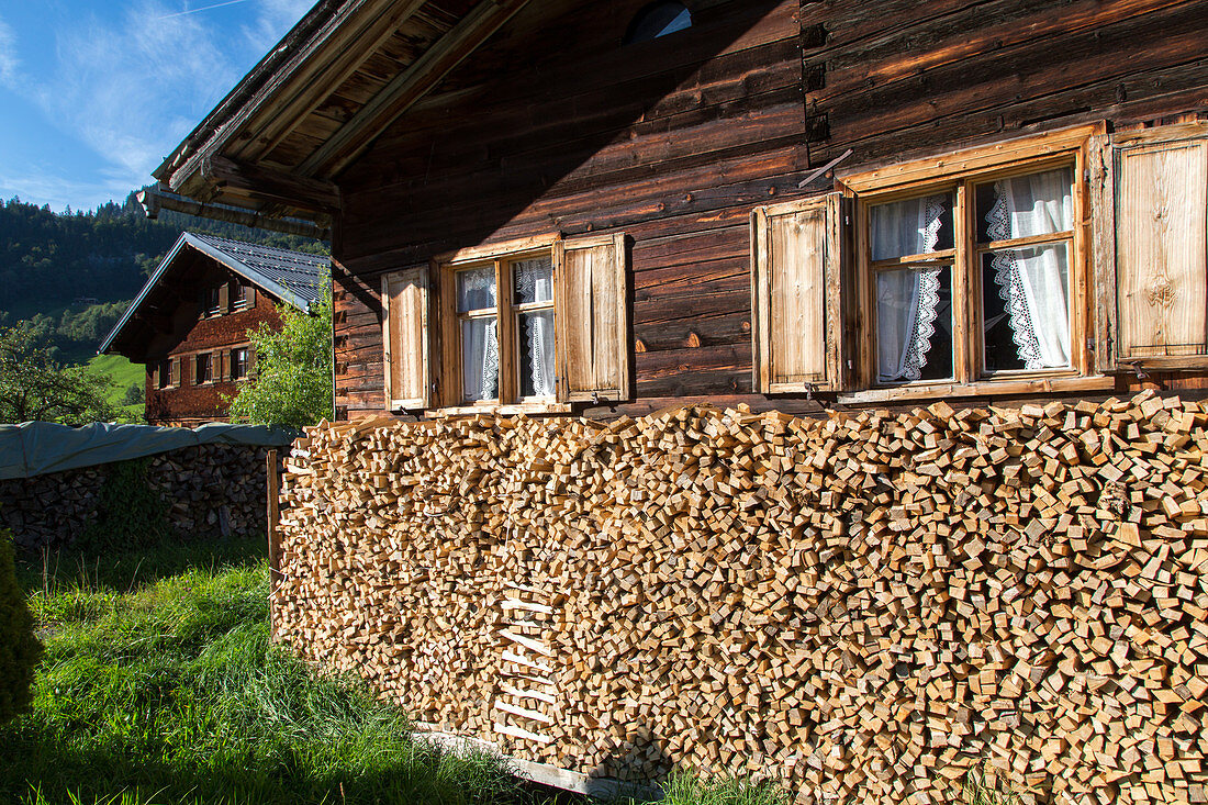 old traditional timber house, firewood stacked below windows with wooden shutters, Bregenzerwald, Vorarlberg, Austria