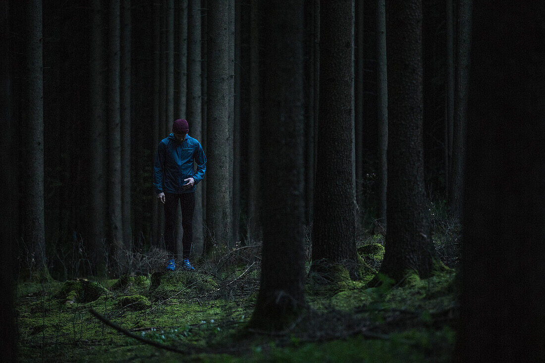 Junger Läufer steht im Wald und sieht nach unten, Allgäu, Bayern, Deutschland