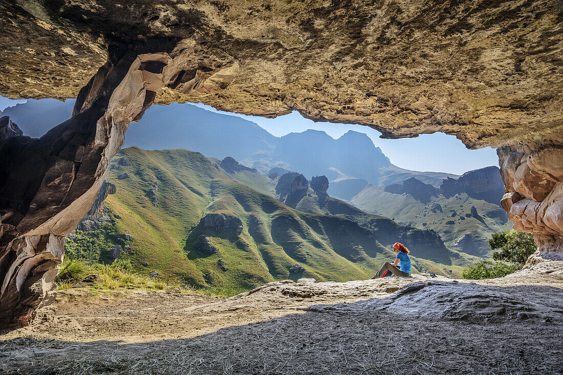 Frau beim Wandern sitzt vor großer Höhle, Pillar Cave, Garden Castle, Mzimkhulu Wilderness Area, Drakensberge, uKhahlamba-Drakensberg Park, UNESCO Welterbe Maloti-Drakensberg-Park, KwaZulu-Natal, Südafrika