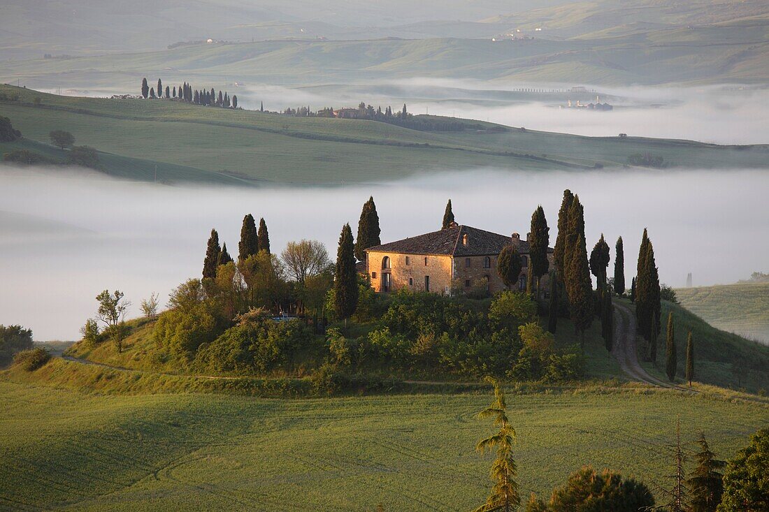 The Belvedere farmhouse in Val d’Orcia with early morning fog, San Quirico d´Orcia, Tuscany, Italy.