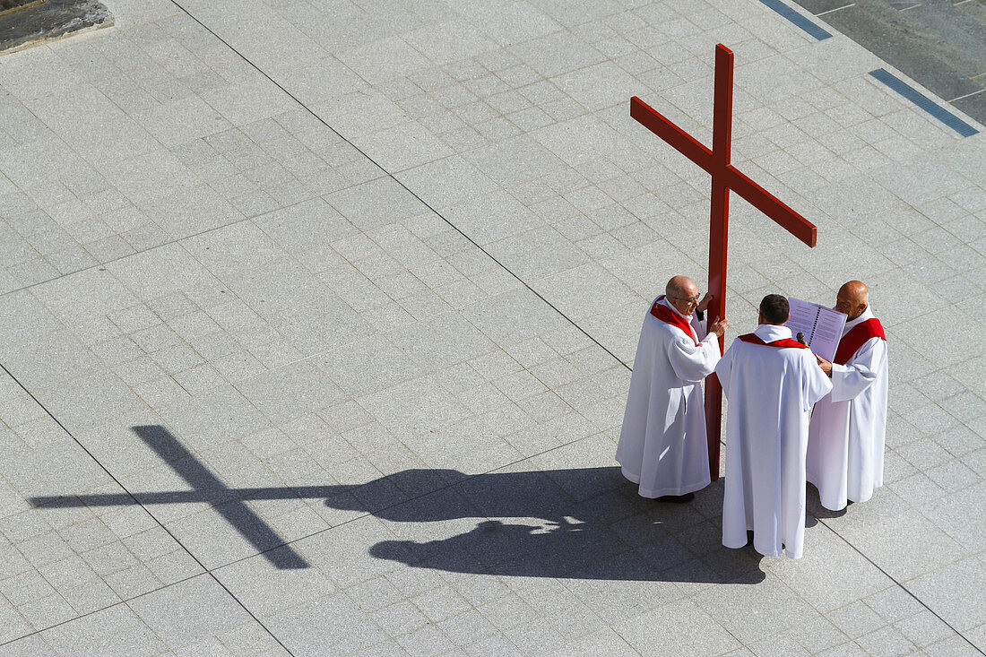 Priest with a cross in Holy Week. Rosary Basilica square. Lourdes city.