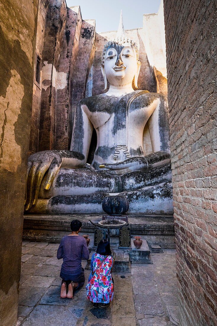 Asia. Thailand, old capital of Siam. Sukhothai archaeological Park, classified UNESCO World Heritage. Wat Si Chum. Couple kneeling praying in front of Buddha statue.