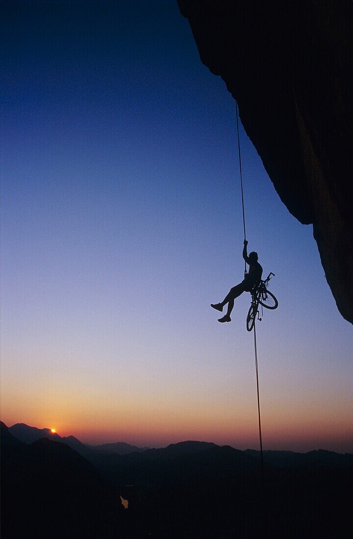 Young man rappeling with his mountain bike.