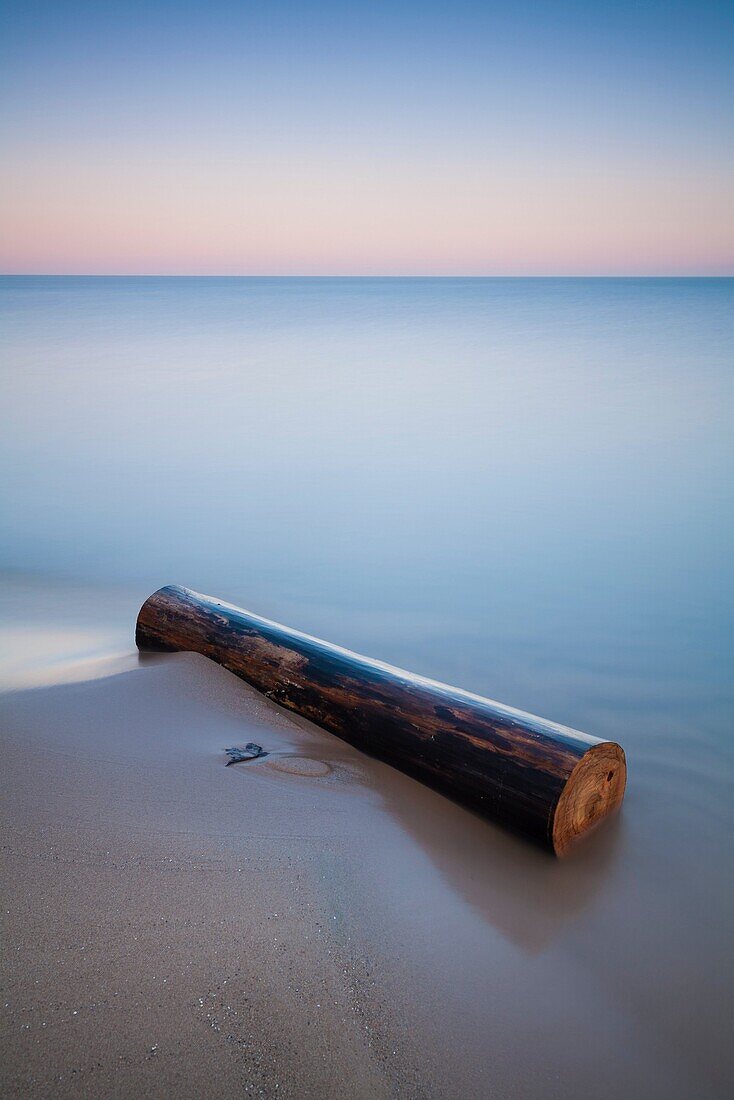 A long exposure creates a soft feel and mood to this image of a log washed ashore on a beach. Pinery Provincial Park, Ontario, Canada.