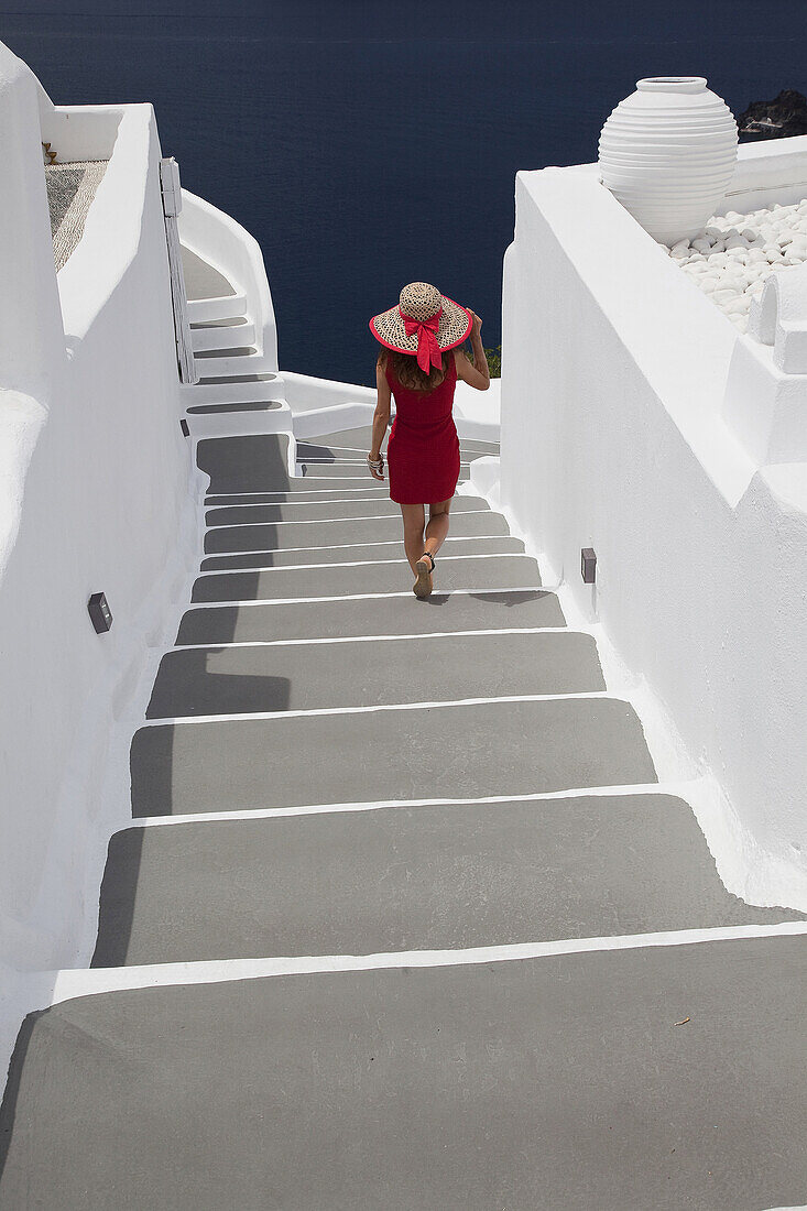 Woman walking down the stairs in Oia town, Santorini, Cyclades Islands, Greek Islands, Greece, Europe.