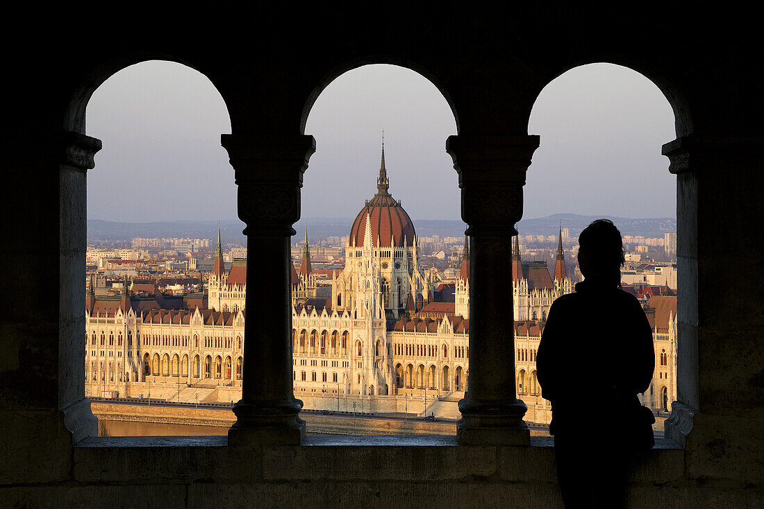 Silhouette of a woman watching the Hungarian Parliament Building from the Fisherman´s Bastion at sunset. Hungary, Budapest. Model Released.