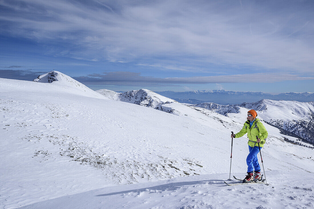 Woman back-country skiing ascending to Eisenhut, Karawanken range in background, Eisenhut, Nock Mountains, Biosphaerenpark Nockberge, Carinthia, Austria