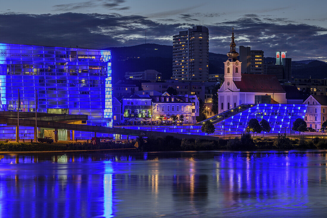 Illuminated Ars Electronica Center and church of Urfahr with Danube in foreground, Linz, Danube Bike Trail, Upper Austria, Austria