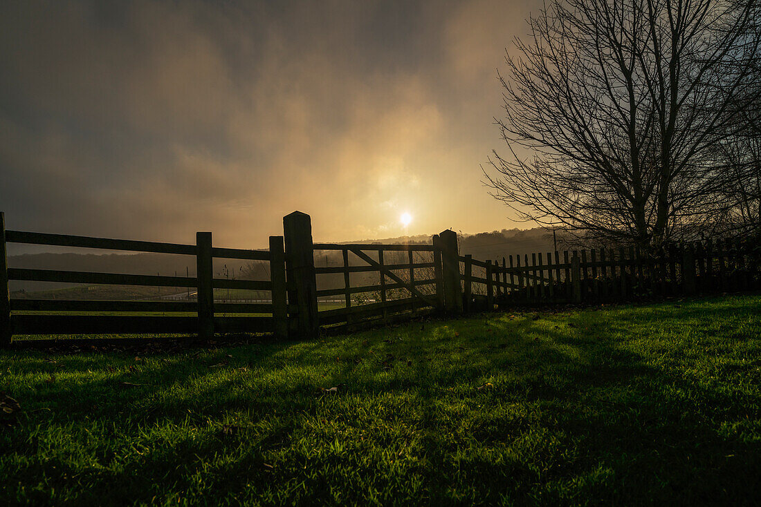 'Sunlight shining through the clouds and a shadow of a fence cast on the grass; Beamish, England'