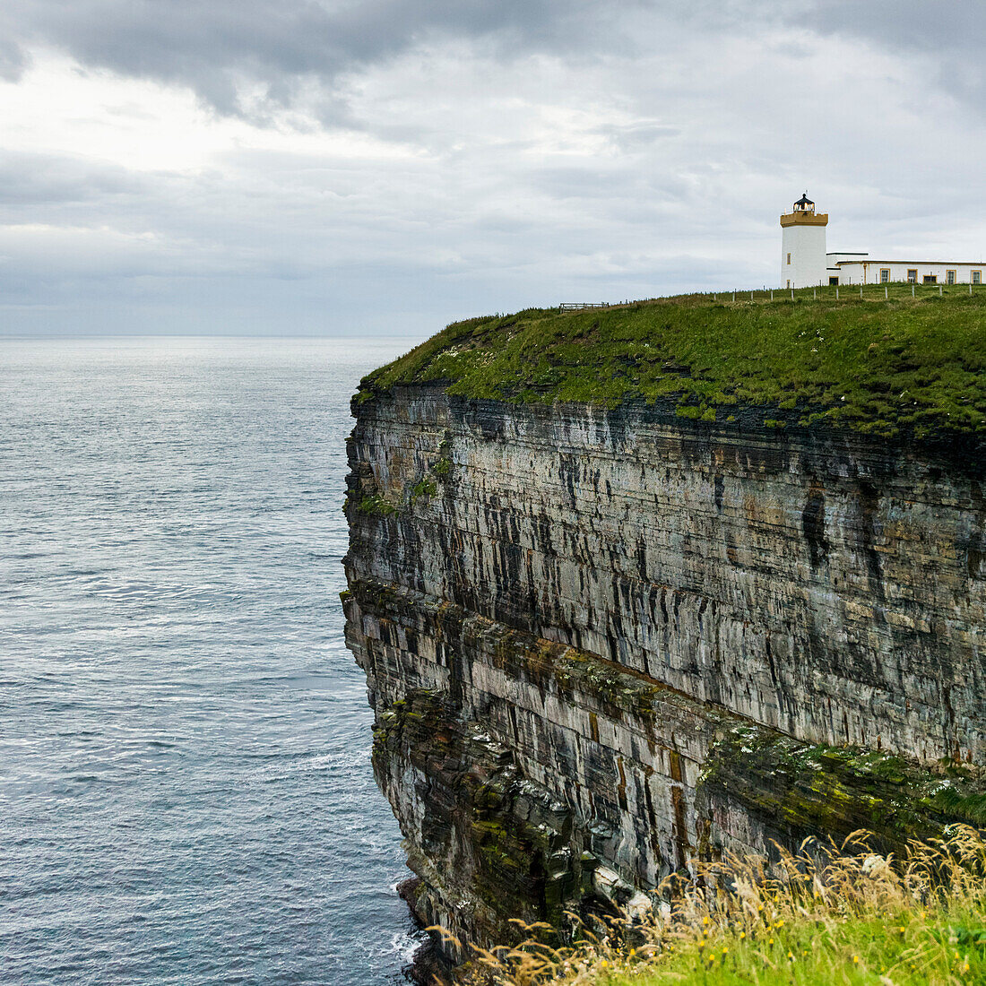 'Duncansby Head Lighthouse on the edge of a cliff on the coast under a cloudy sky; Scotland'