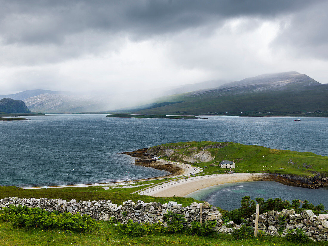 'A beach and green landscape with low clouds over the mountains in the distance; Scotland'