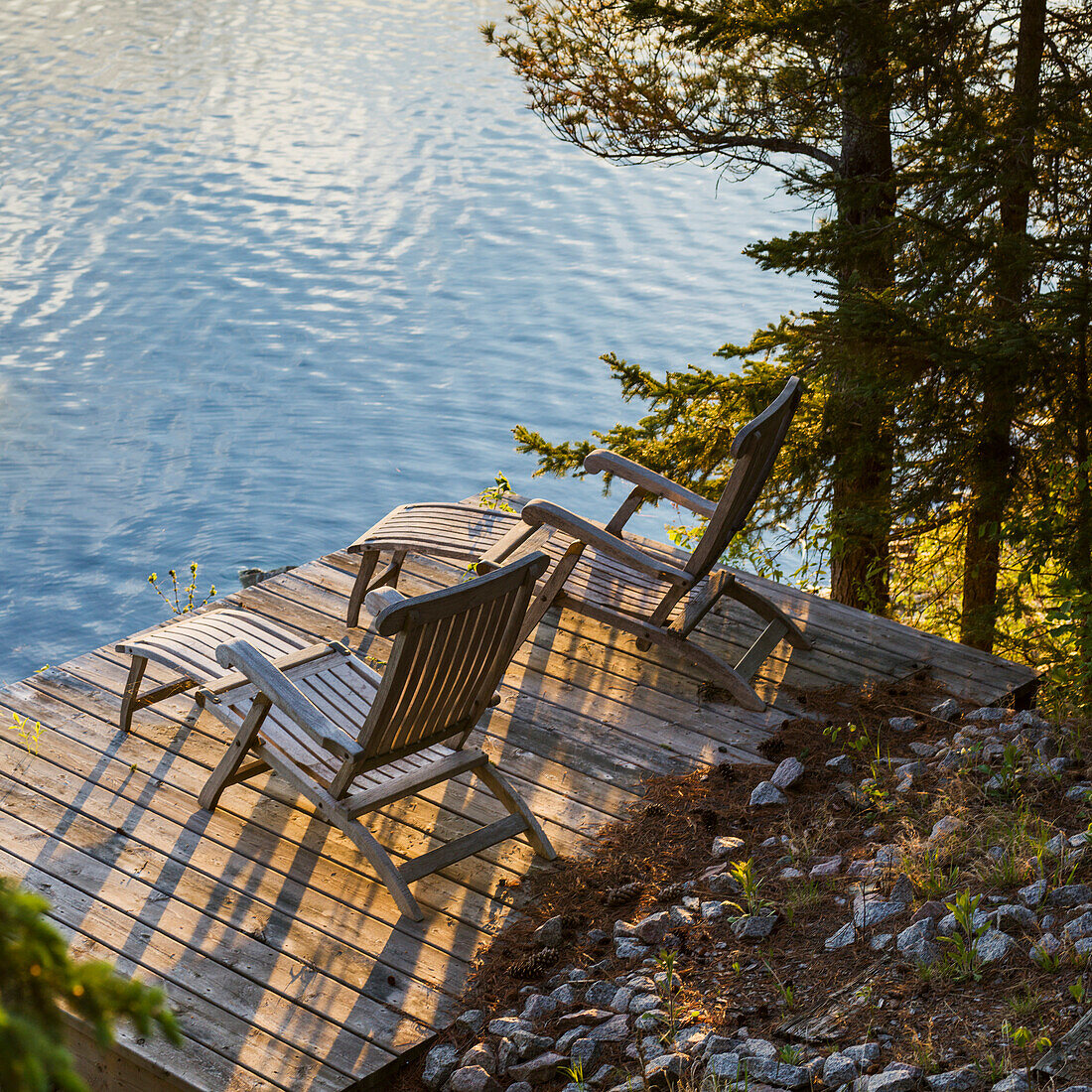 'Two wooden lounge chairs on a dock looking out at Lake of the Woods at dusk; Ontario, Canada'
