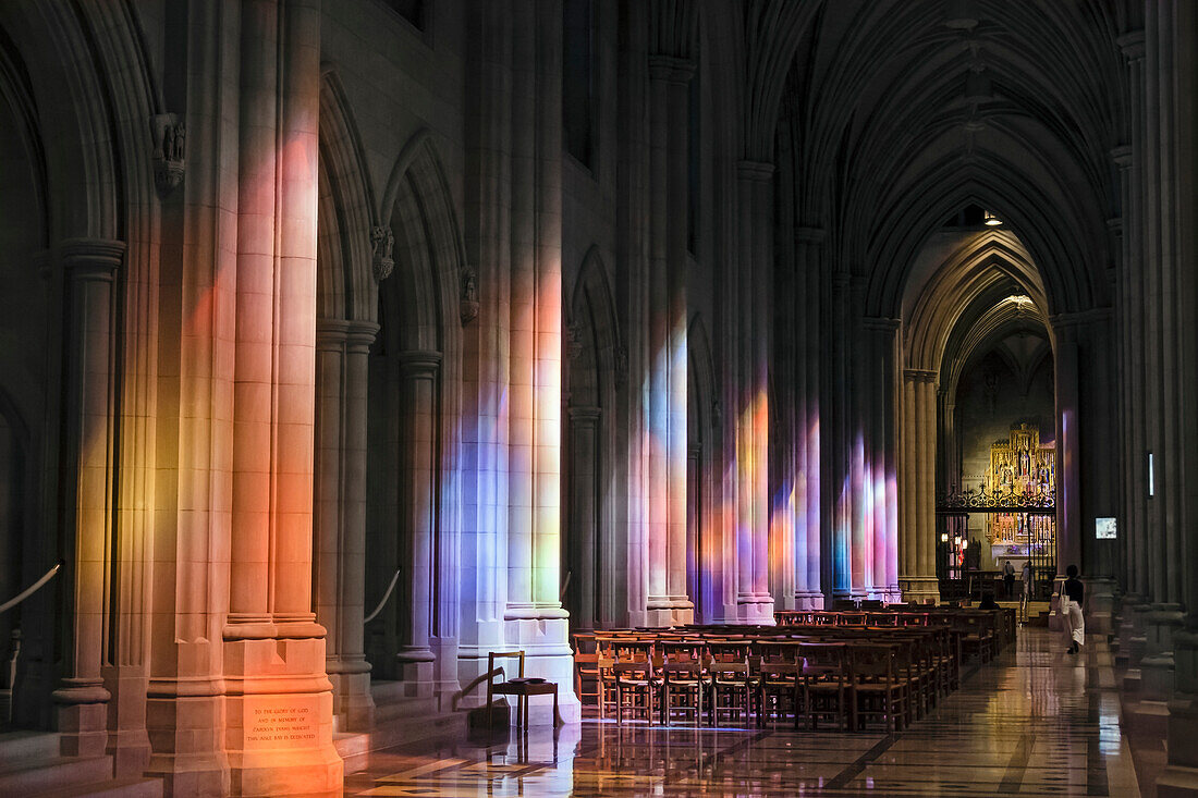 'Light streaming through stained glass windows with colourful light columns along the cathedral nave, altarpiece in St. Mary's Chapel visible background; Washington, District of Columbia, United States of America'