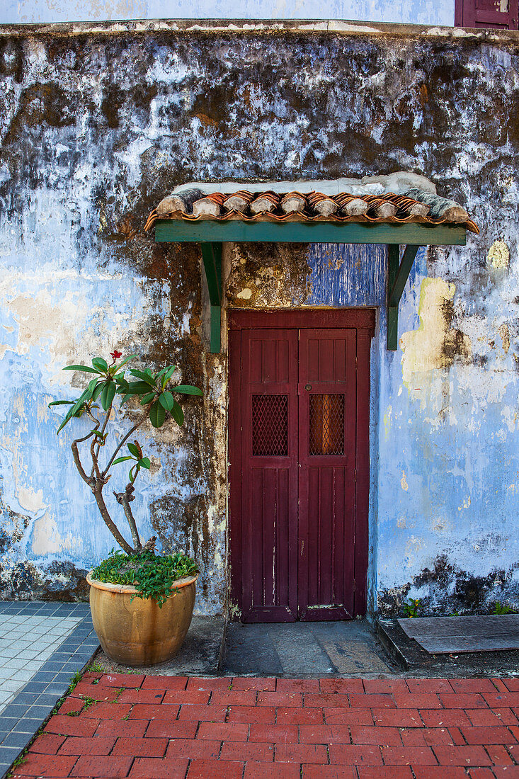 'A faded red door sits surrounded by a weathered blue wall in downtown Georgetown; Georgetown, Penang, Malaysia'