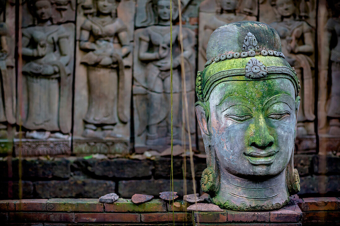 'A terra cotta head of buddha sits in front of bas-relief in a terra cotta garden; Chiang Mai, Thailand'