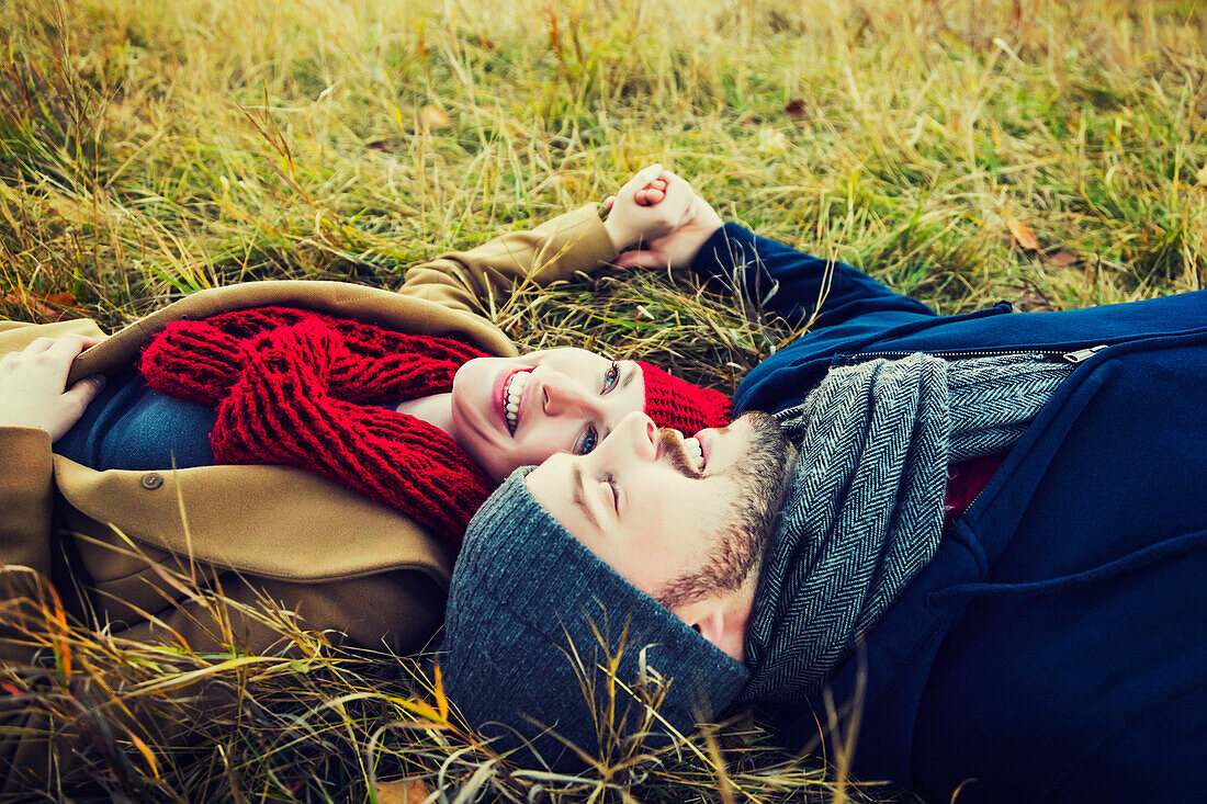 'A young couple laying in the grass and holding hands in a park in autumn; Edmonton, Alberta, Canada'