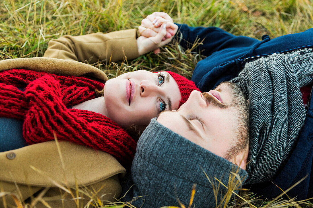 'A young couple laying in the grass and holding hands in a city park in autumn; Edmonton, Alberta, Canada'