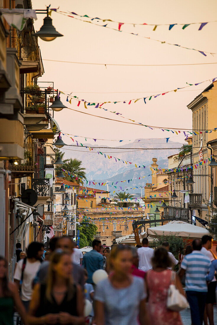 'Tourists walking down a busy street at dusk; Olbia, Sardinia, Italy'