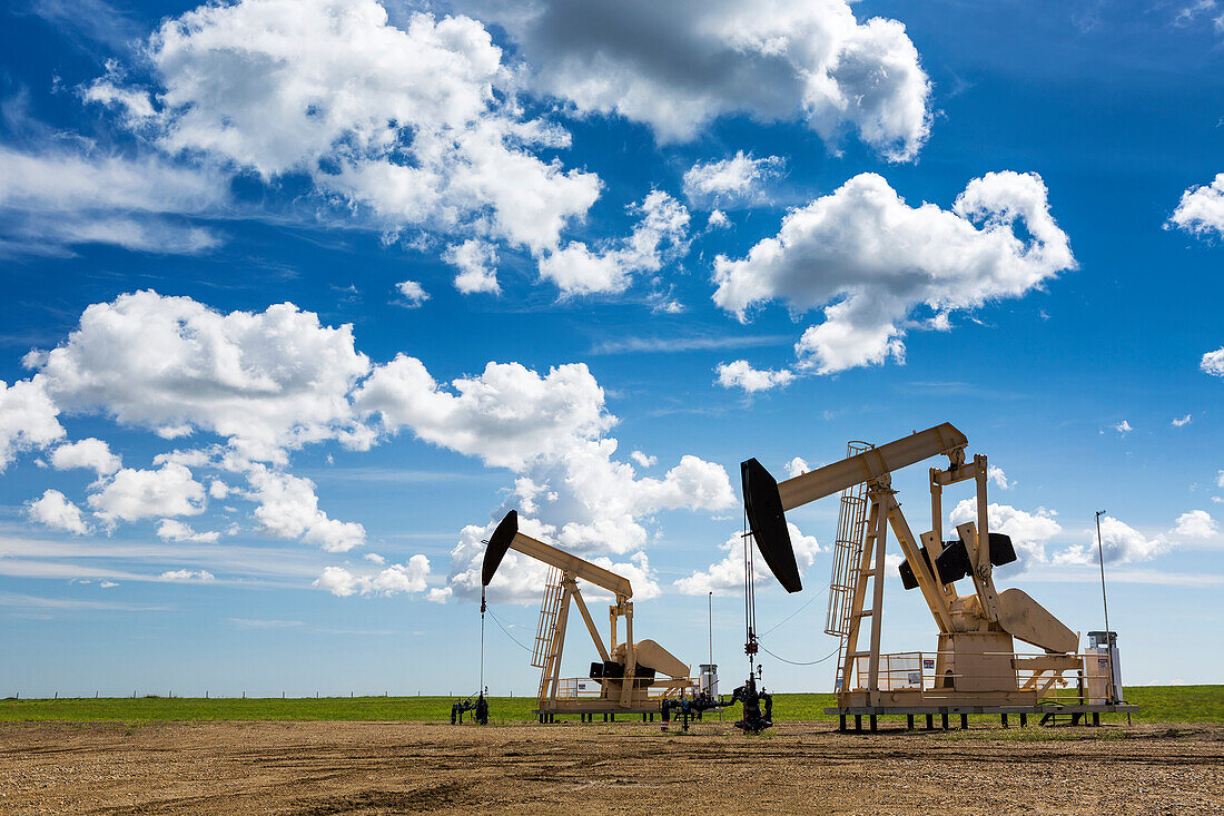 'Two pump jacks in a field with large puffy clouds and blue sky; Alberta, Canada'