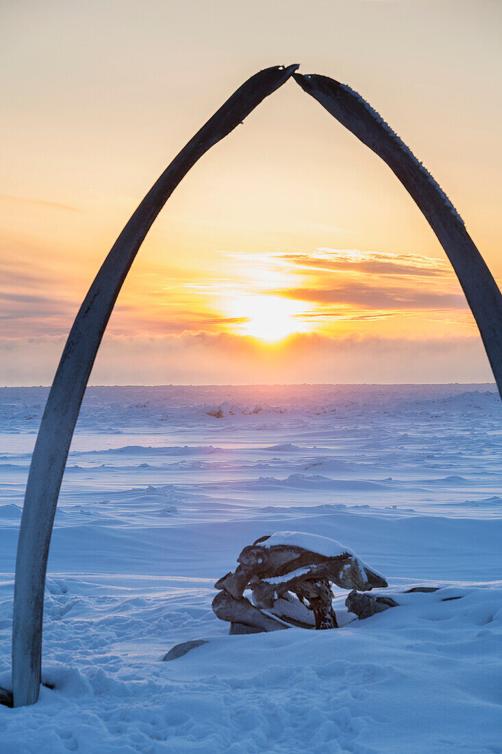 Whalebone arch frames the setting sun at the shore of the Arctic Ocean in Barrow, North Slope, Arctic Alaska, Winter