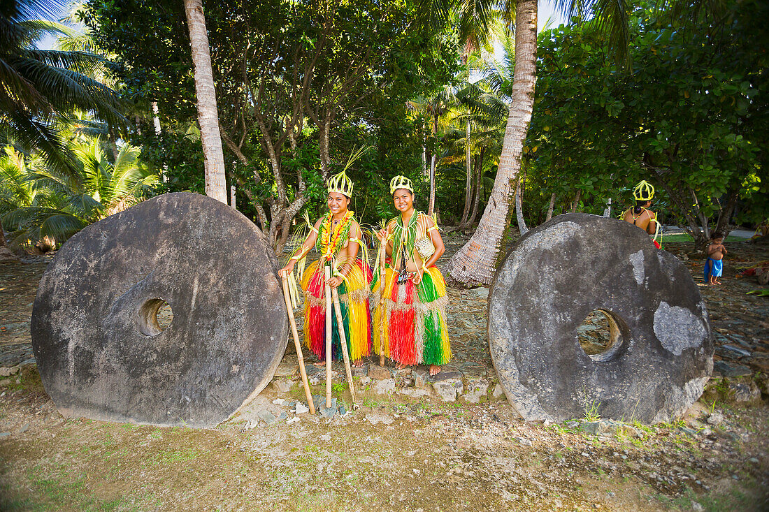 'These two young girls between the two pieces of stone money, are in a traditional outfit for cultural ceremonies on the island of Yap; Yap, Federated States of Micronesia'