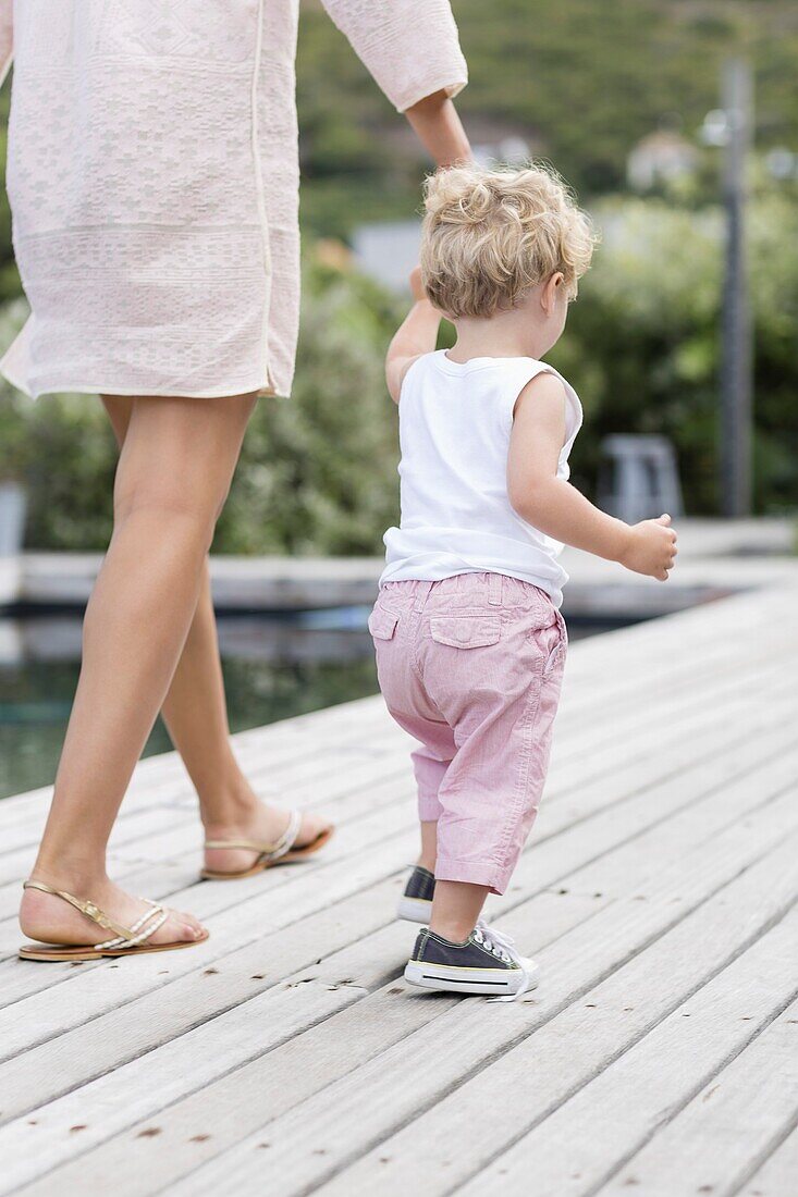 Rückansicht einer Mutter, die mit ihrem Sohn am Pool spazieren geht