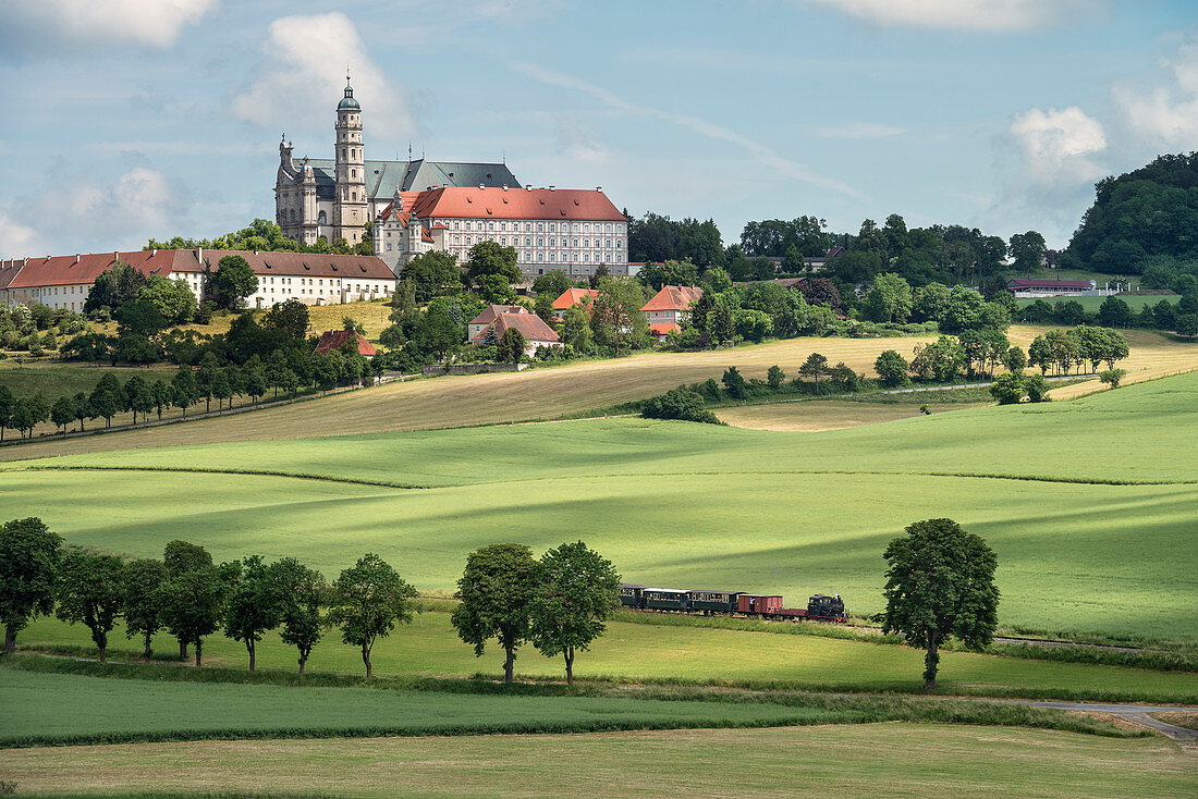 historical steam train passes Benedictine abbey at the so called Haertsfeld, Neresheim monastry, Ostalb district, Swabian Alb, Baden-Wuerttemberg, Germany