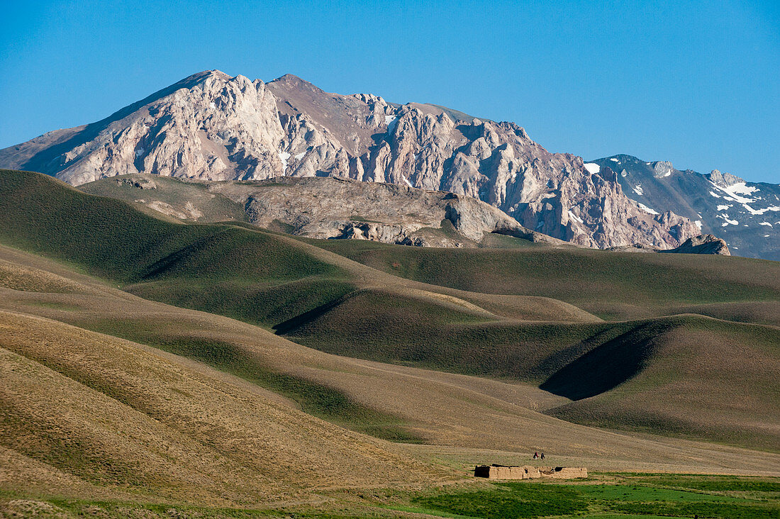 A distant house in the grasslands with views of mountains in the distance, Bamiyan province, Afghanistan, Asia