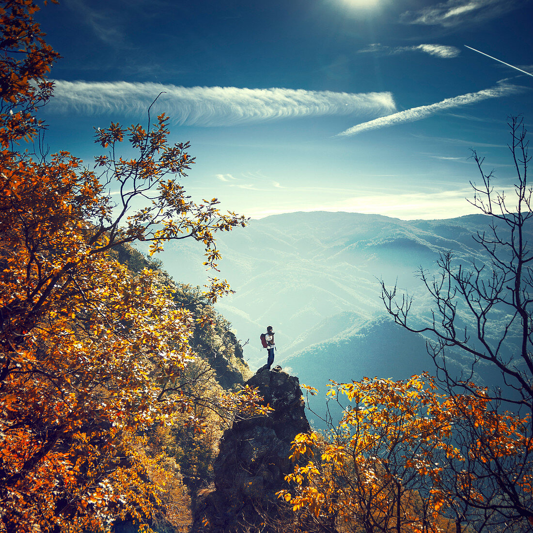 Look through forest on a hiker standing on narrow rock pointing up from hill side Shot on mountain Stolovi, Serbia