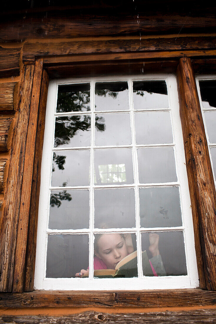 Young girl reads next to cabin window