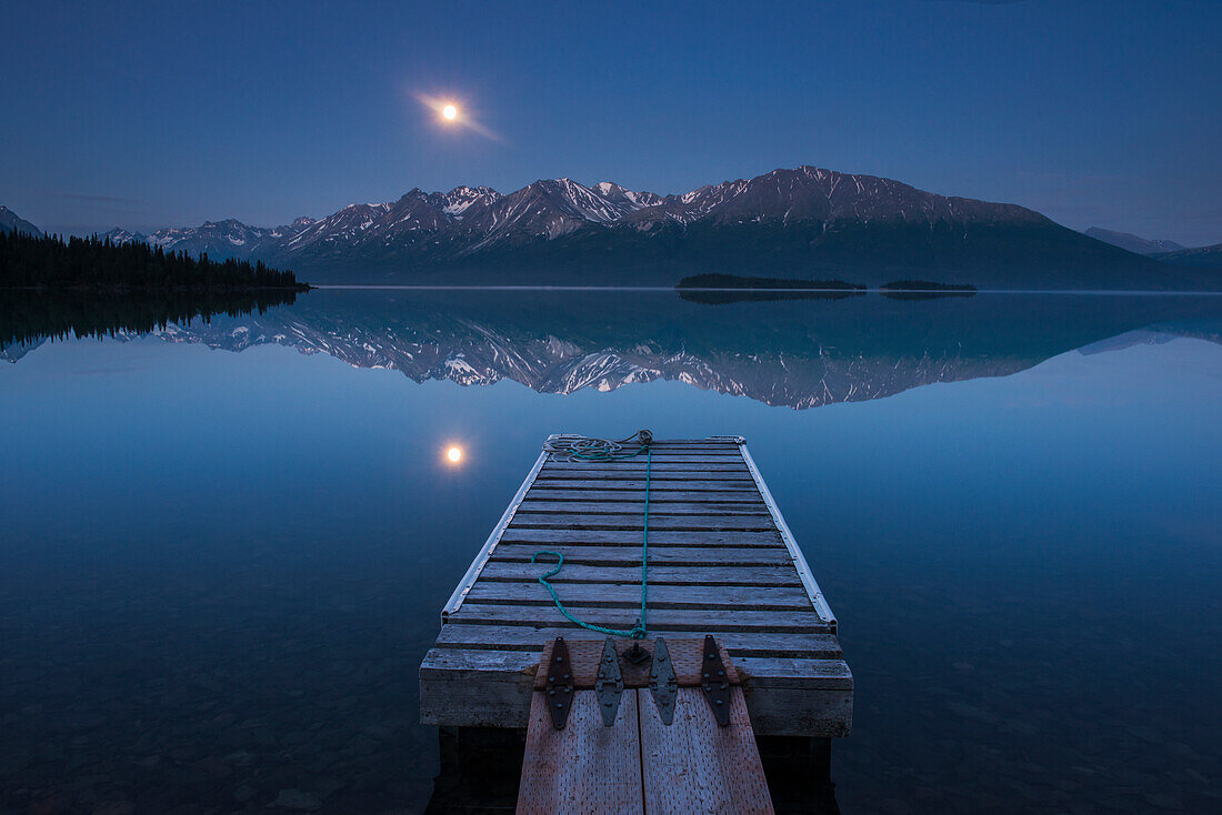 Boat dock with a full moon rising over the Chigmit Mountains at Lake Clark in Lake Clark National Park and Preserve, Alaska.